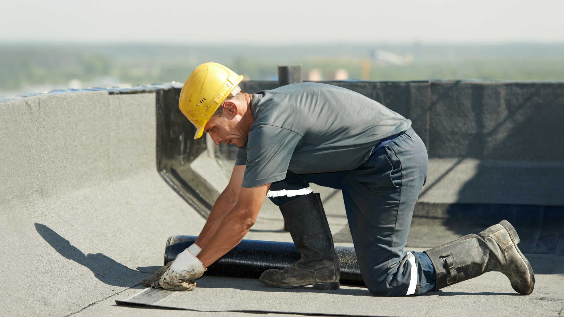 Construction worker in a yellow hard hat inspecting the flat roof